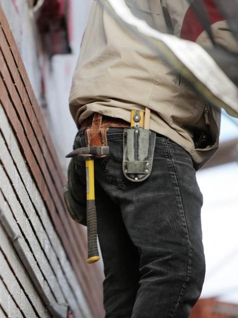 Compagnon de dos, ceinture à outils et marteau, le long d'un mur en cours de dépose