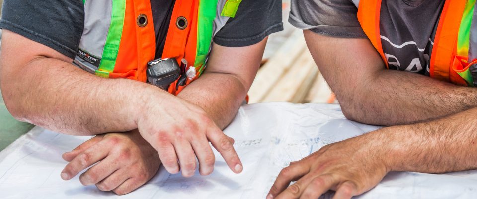 Trois compagnons en gilet haute visibilité penchés sur les plans d'un chantier